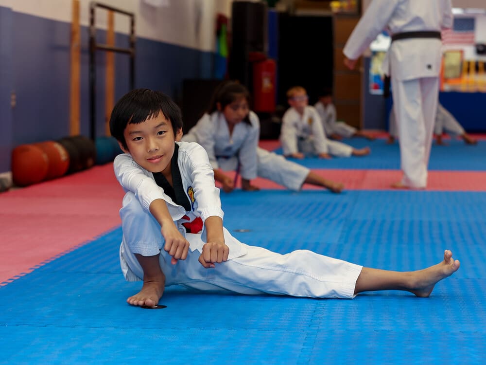 a kid in taekwondo uniform stretching on blue mat with joy in Norristown PA